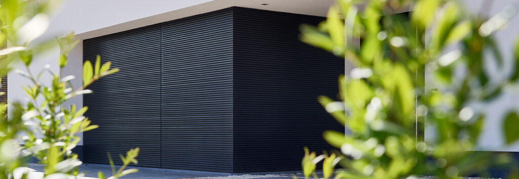 Corrugated garage door partially blocked by leafy plants.